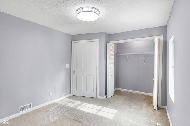 unfurnished bedroom with a closet, light colored carpet, and a textured ceiling