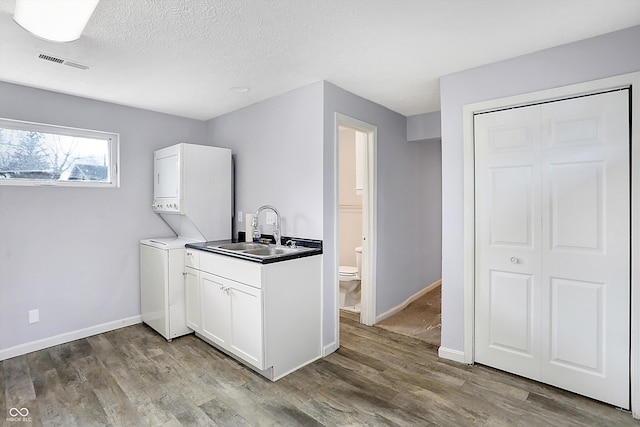 kitchen featuring sink, stacked washer / dryer, wood-type flooring, a textured ceiling, and white cabinets