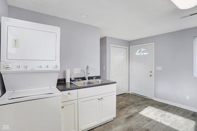 laundry room featuring wood-type flooring, a textured ceiling, stacked washer and clothes dryer, and sink