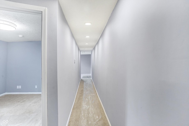 corridor with a textured ceiling and light colored carpet