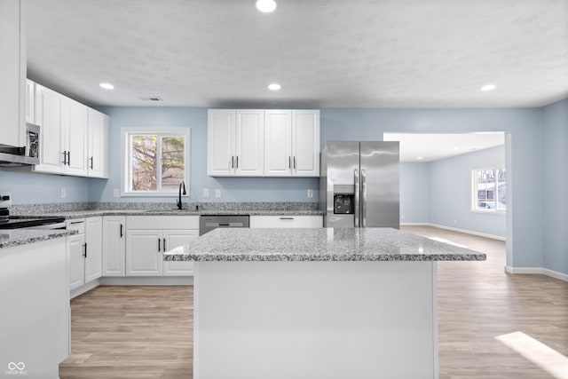 kitchen featuring white cabinets, a kitchen island, stainless steel appliances, and light hardwood / wood-style flooring