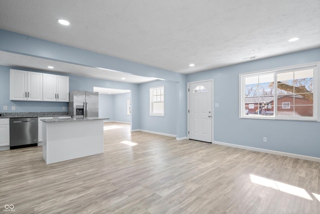 kitchen with appliances with stainless steel finishes, white cabinetry, a kitchen island, and a wealth of natural light