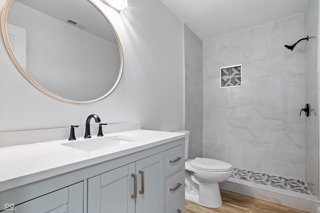 bathroom with hardwood / wood-style flooring, vanity, toilet, and a tile shower