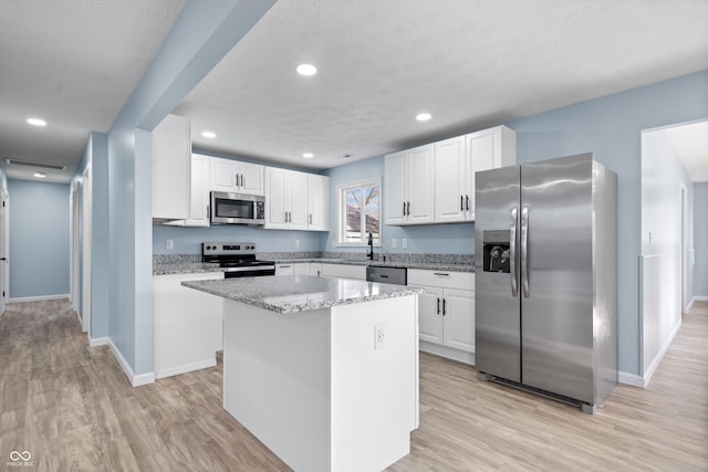 kitchen with a center island, a textured ceiling, appliances with stainless steel finishes, light hardwood / wood-style floors, and white cabinetry