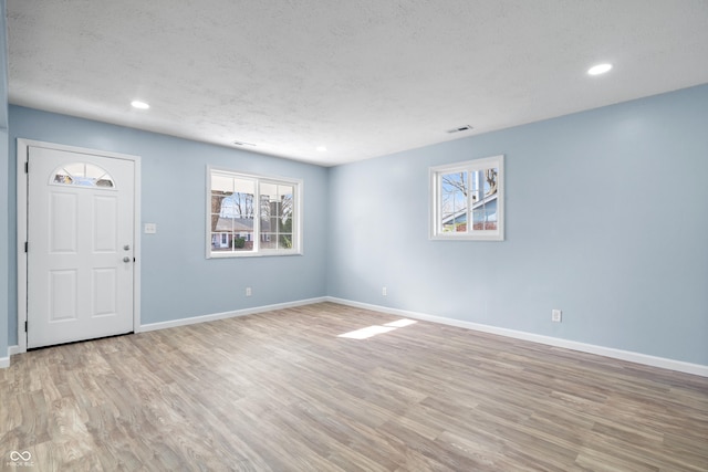 spare room featuring a wealth of natural light, a textured ceiling, and light wood-type flooring