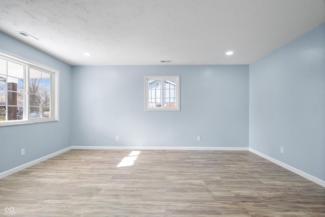 empty room with a textured ceiling, light hardwood / wood-style floors, and a healthy amount of sunlight