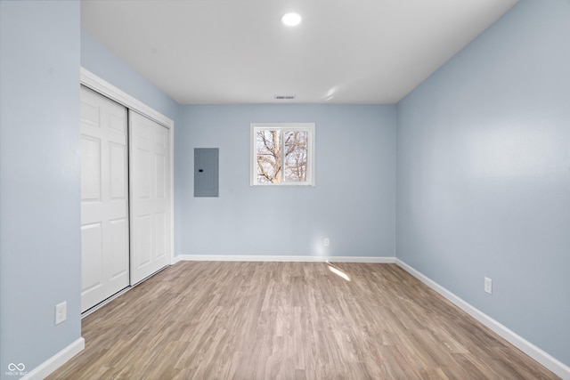 unfurnished bedroom featuring electric panel, light hardwood / wood-style floors, and a closet