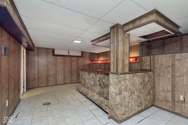 bar with a paneled ceiling, wooden walls, and light tile patterned floors