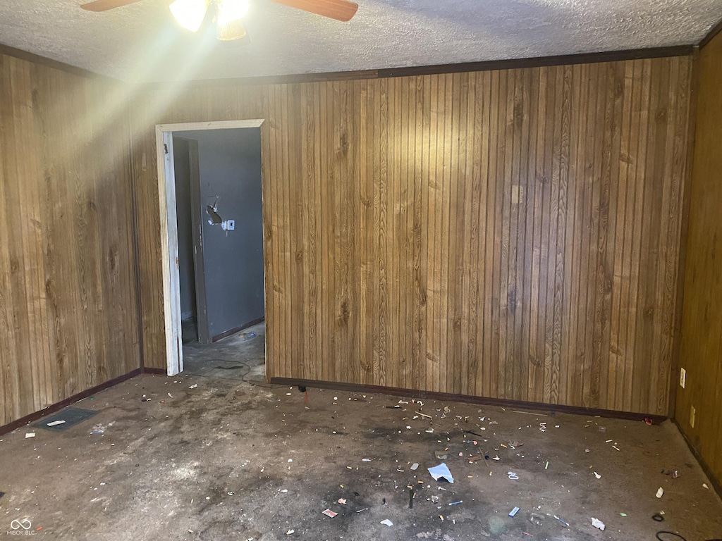 spare room with wood walls, ceiling fan, and a textured ceiling