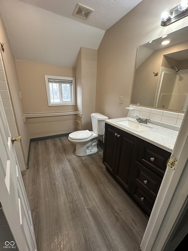 bathroom with vanity, toilet, wood-type flooring, and vaulted ceiling