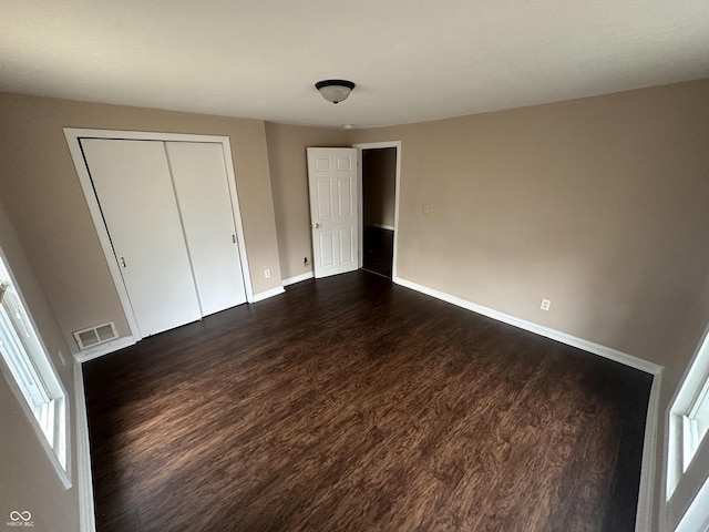 unfurnished bedroom featuring multiple windows, dark wood-type flooring, and a closet