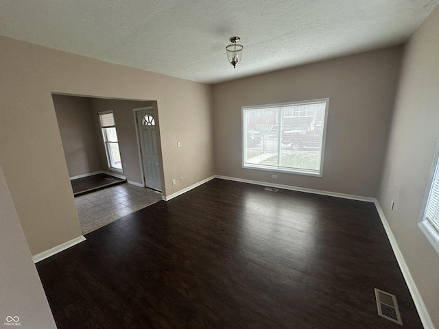 unfurnished room with a wealth of natural light, dark hardwood / wood-style flooring, and a textured ceiling