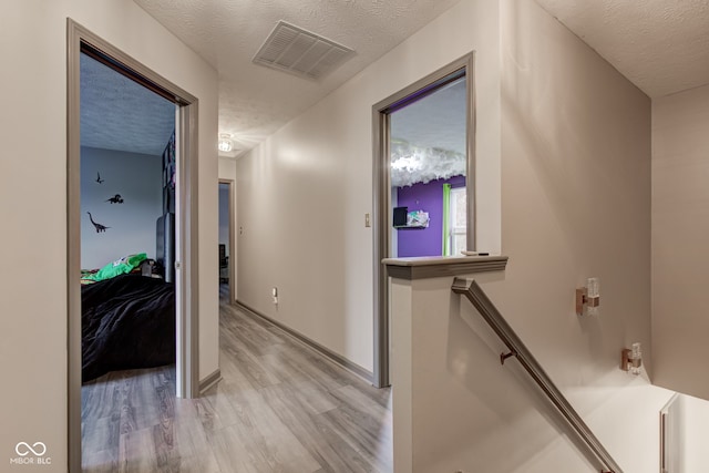 corridor with light wood-type flooring and a textured ceiling