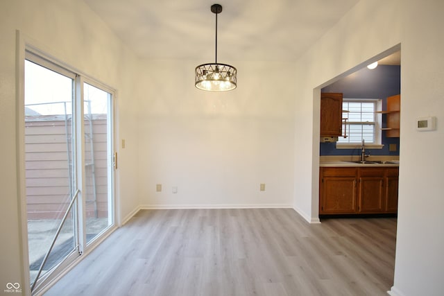 unfurnished dining area with a healthy amount of sunlight, light hardwood / wood-style floors, sink, and a chandelier