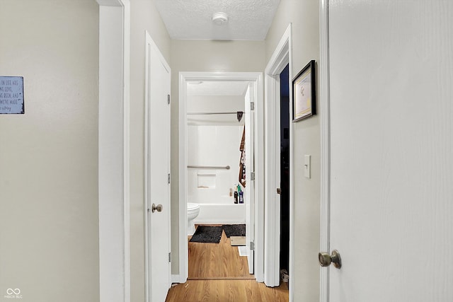 hallway with light wood-type flooring and a textured ceiling