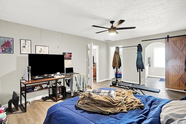 bedroom featuring a barn door, ceiling fan, a textured ceiling, and hardwood / wood-style flooring