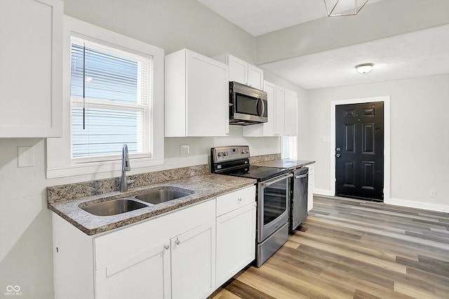 kitchen with sink, white cabinetry, light hardwood / wood-style flooring, dark stone countertops, and appliances with stainless steel finishes