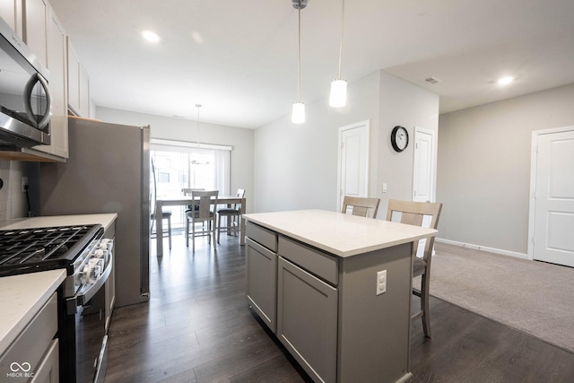 kitchen with gray cabinetry, a breakfast bar, hanging light fixtures, dark hardwood / wood-style floors, and appliances with stainless steel finishes