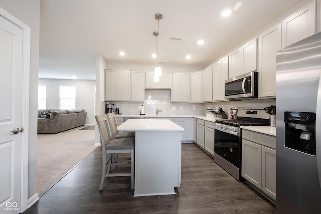 kitchen with a breakfast bar, hanging light fixtures, appliances with stainless steel finishes, and dark wood-type flooring