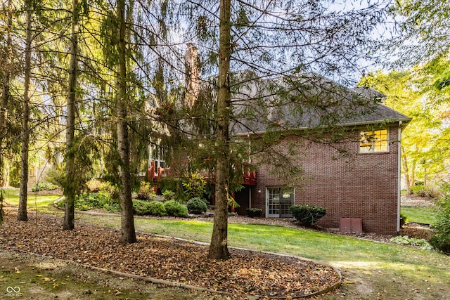 exterior space featuring brick siding, a shingled roof, and a front lawn