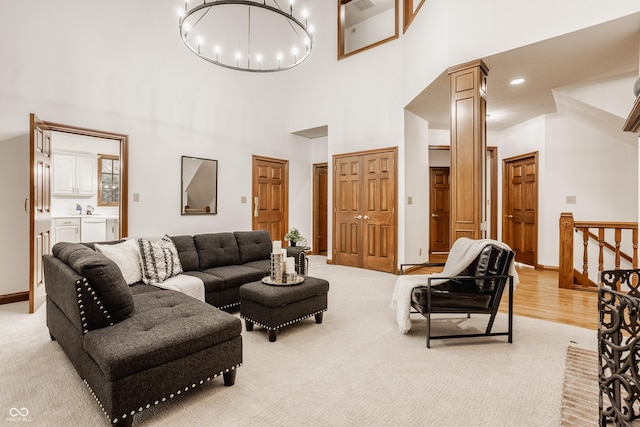 living room with baseboards, ornate columns, a towering ceiling, a notable chandelier, and light colored carpet