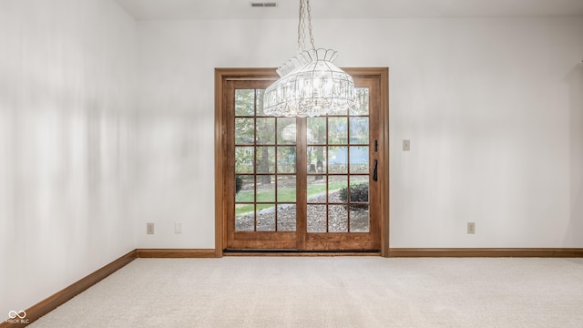 carpeted spare room featuring a notable chandelier, visible vents, and baseboards