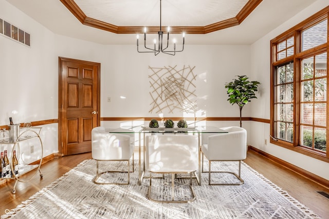 dining area with wood finished floors, baseboards, an inviting chandelier, a tray ceiling, and crown molding