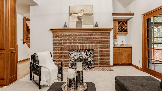 sitting room with baseboards, wet bar, a brick fireplace, and light carpet