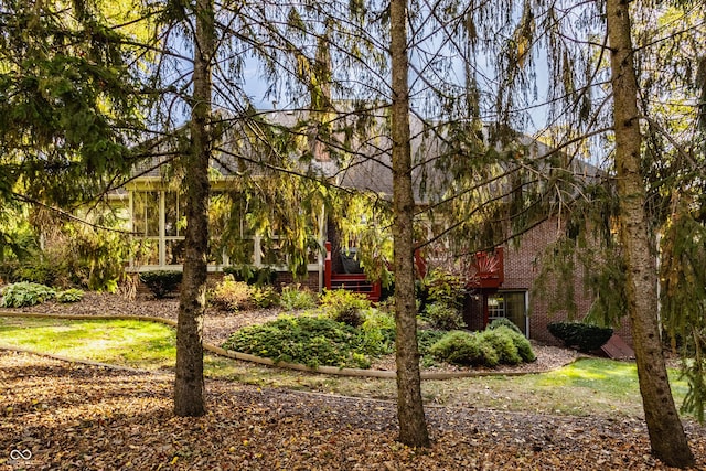 view of property hidden behind natural elements featuring a wooden deck and brick siding