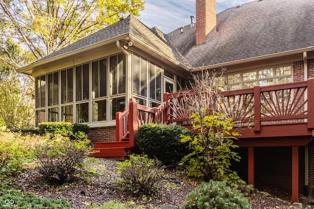 exterior space with roof with shingles, brick siding, a sunroom, and a chimney