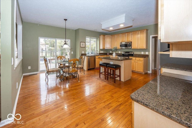 kitchen featuring a breakfast bar area, appliances with stainless steel finishes, light brown cabinets, a kitchen island, and light wood-type flooring