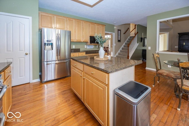 kitchen featuring stainless steel refrigerator with ice dispenser, light brown cabinetry, a kitchen island, and light hardwood / wood-style flooring