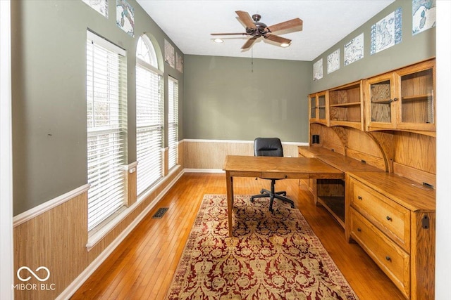 office space featuring ceiling fan, a healthy amount of sunlight, hardwood / wood-style floors, and wood walls