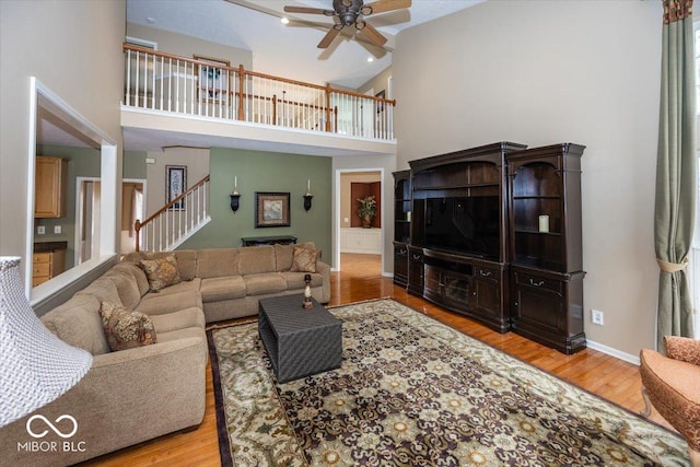 living room with ceiling fan, light hardwood / wood-style flooring, and a high ceiling