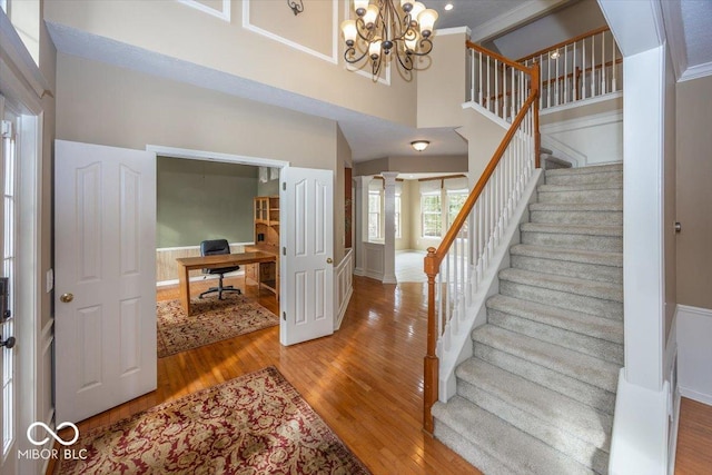 staircase featuring a notable chandelier, wood-type flooring, decorative columns, and a high ceiling