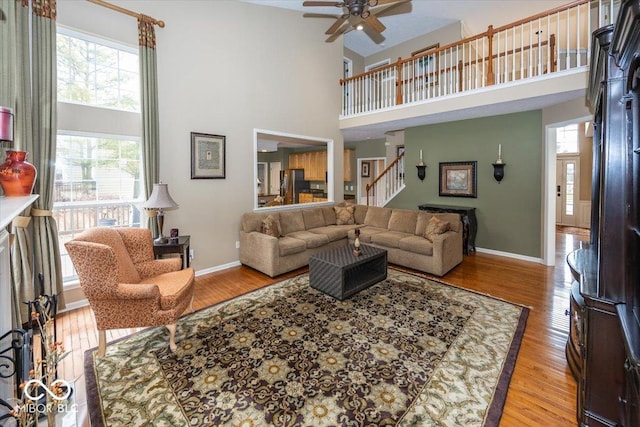 living room with ceiling fan, a towering ceiling, and light wood-type flooring