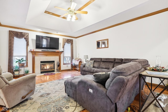 living room with a tile fireplace, a raised ceiling, crown molding, hardwood / wood-style flooring, and ceiling fan