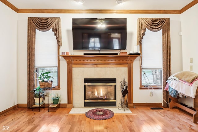 living room with wood-type flooring, ornamental molding, and a tile fireplace