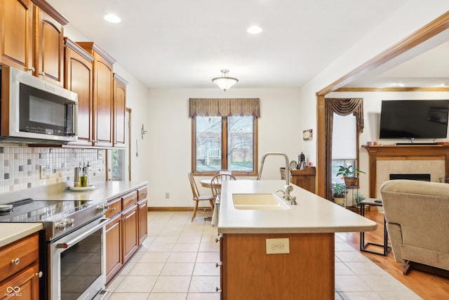 kitchen featuring stainless steel appliances, sink, light tile patterned floors, a center island with sink, and a tiled fireplace