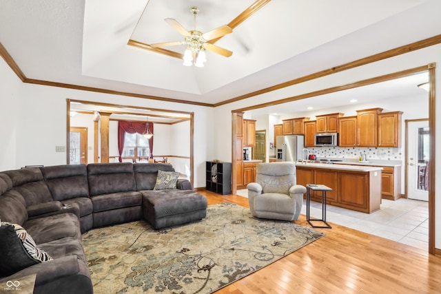 living room featuring ceiling fan, ornamental molding, light hardwood / wood-style flooring, and a tray ceiling