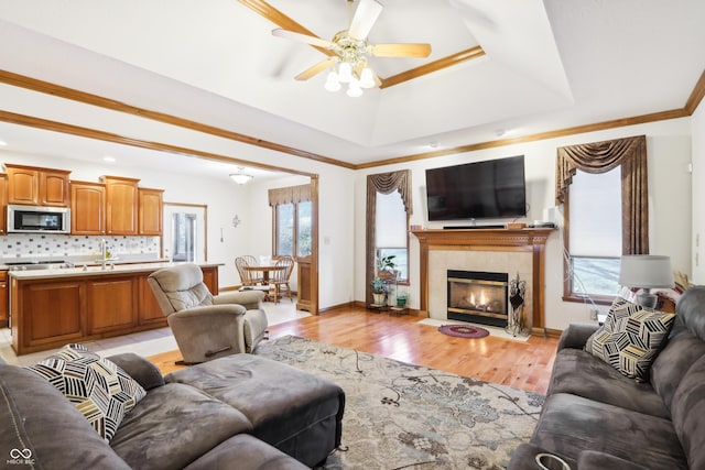 living room featuring ceiling fan, a raised ceiling, light wood-type flooring, a fireplace, and ornamental molding