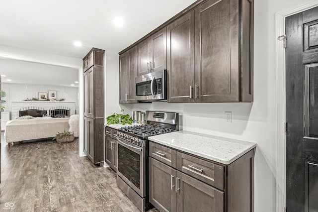 kitchen with dark brown cabinets, light stone countertops, wood-type flooring, and stainless steel appliances