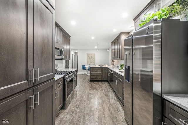 kitchen with kitchen peninsula, dark brown cabinets, stainless steel appliances, wood-type flooring, and hanging light fixtures