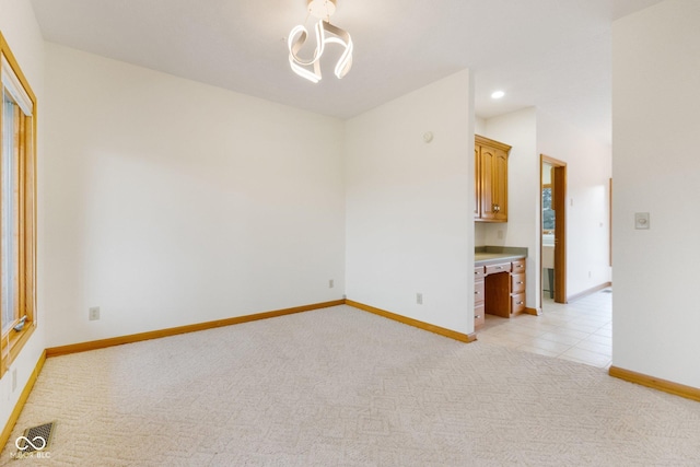 spare room with light colored carpet, built in desk, and an inviting chandelier