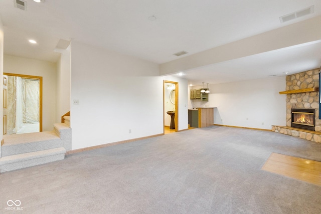 unfurnished living room featuring a stone fireplace and light colored carpet