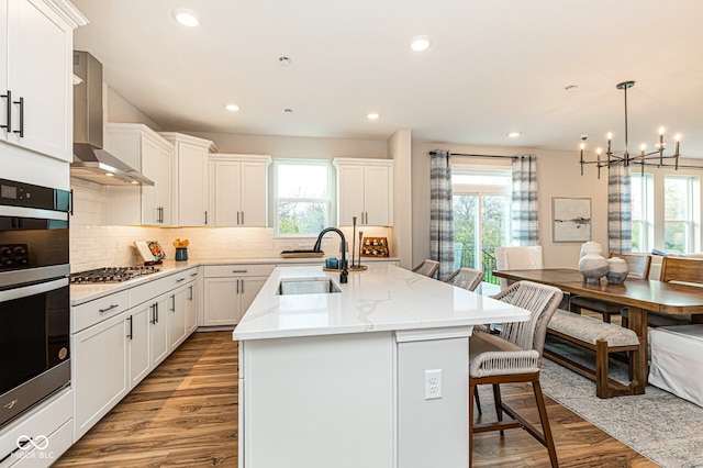 kitchen with a wealth of natural light, sink, wall chimney exhaust hood, and an island with sink