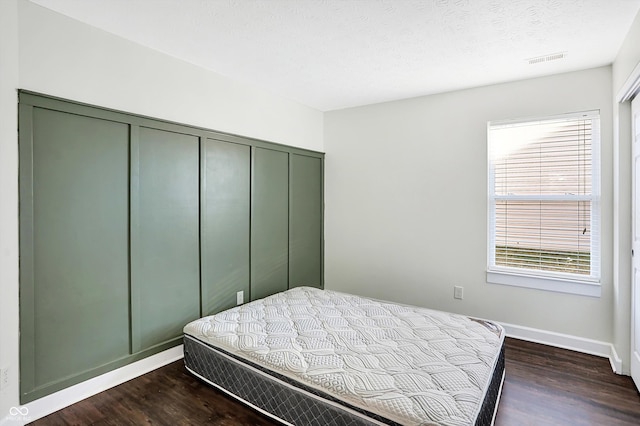 bedroom with dark hardwood / wood-style floors, a textured ceiling, and a closet