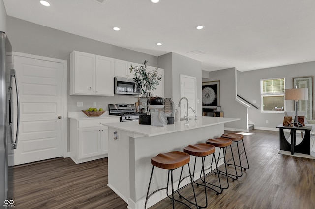 kitchen with white cabinets, appliances with stainless steel finishes, dark hardwood / wood-style flooring, and a kitchen island with sink