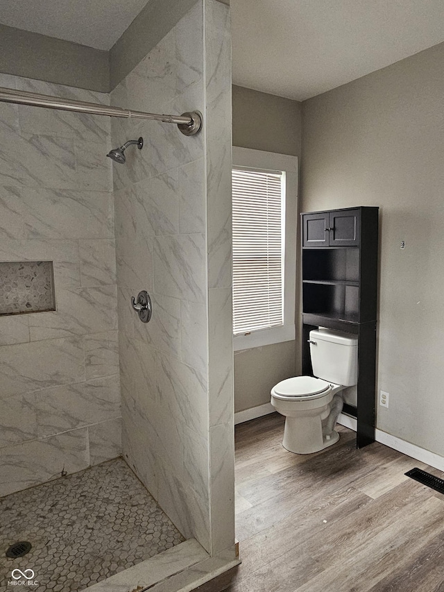 bathroom featuring toilet, wood-type flooring, and tiled shower