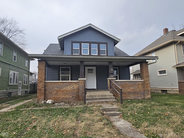 bungalow-style house featuring a front yard, covered porch, brick siding, and roof with shingles